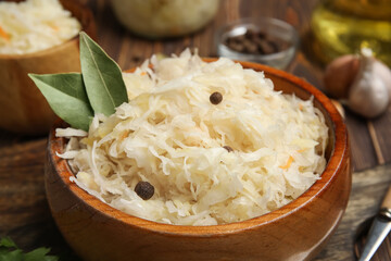 Bowl of delicious sauerkraut with bay leaves and peppercorn on wooden background