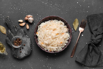 Bowl with delicious sauerkraut and different spices on black background