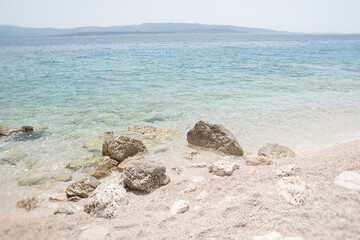 Boulders washed by turquoise color sea with island on horizon.