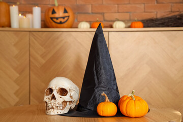 Halloween pumpkins with witch hat and skull on table in living room, closeup