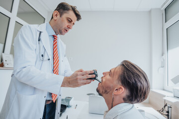 Obraz premium Experienced Doctor Examining Elderly Patient's Ears, Eyesight, and Throat in Clinic