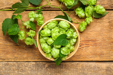 Bowl with fresh green hops and leaves on wooden background