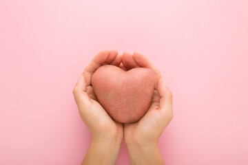 Heart shape of fresh big potato in young adult woman opened palms on light pink table background....
