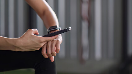Young female athlete in sportswear sits at the gym using a cell phone while relaxing.