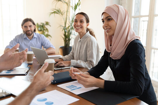 Group of multicultural businesspeople listens associates diverse staff take part in briefing sit at desk do financial analysis, listen speech of ceo analysing sales growth finances positive statistics