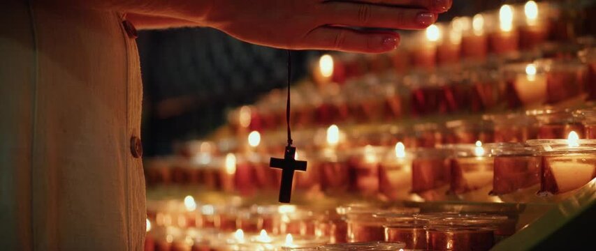 Woman praying in church. Adult girl clasping hands with cross near burning candles.