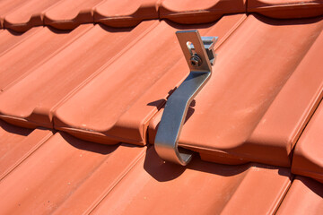 Dachdecker beim Aufbau einer Photovoltaikanlage auf einem neu gedeckten Ziegeldach: Justage und Verschraubung der Klemmen für das Schienensystem an den Dachsparren - obrazy, fototapety, plakaty