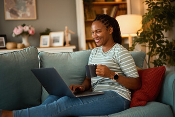 Happy african american woman with laptop and coffee at home