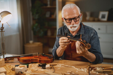 Senior carpenter craftsman carving wood and making violin instrument