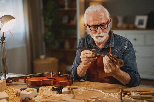Senior carpenter craftsman carving wood and making violin instrument