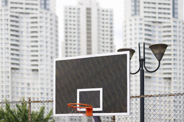 basketball board with orange hoop and damaged net. Urban skycraper background.