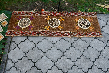 A close up on a decorations made out of autumn leaves, cones, herbs, and other kinds of flora located next to a pavement and a small public park seen on a sunny summer day in Poland