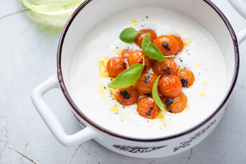 Greek feta dip sauce with roasted cherry tomatoes and fresh basil in a white serving pan, middle...