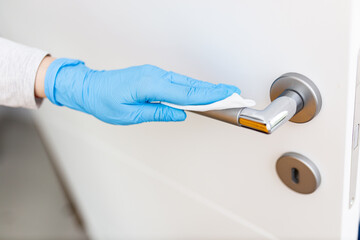 Close up of female hand in blue protective glove cleaning door handle with wipe, healthcare concept.