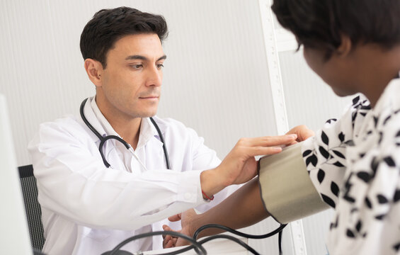 Hispanic doctor measuring African American patient's blood pressure. Person medical healthcare and wellbeing, the physician meet with patient at clinic concept.