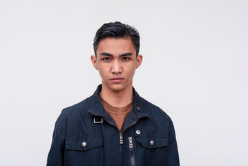 A serious young Filipino teen in a black jacket, jeans and white sneakers. Isolated on a white background.