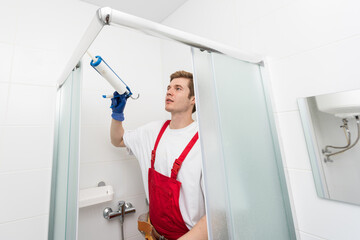 Naklejka na ściany i meble Workers are installing a silicone gasket seal on the glass door of the shower enclosure.