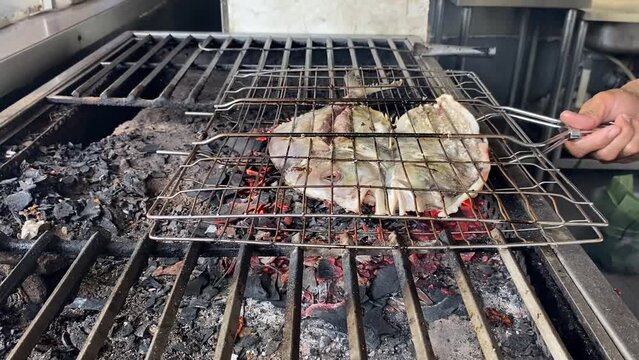 The pompano fish that has been cut in half is grilled over coals using charcoal at restaurant.	