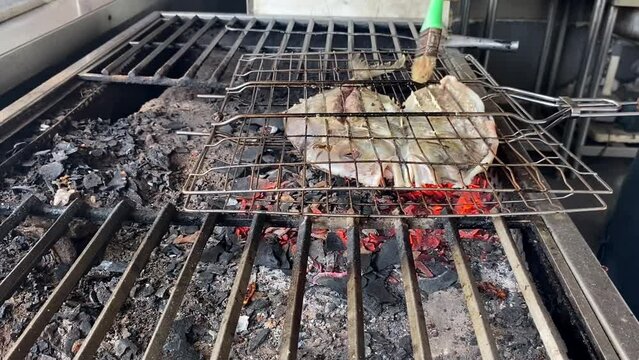 The pompano fish that has been cut in half is grilled over coals using charcoal at restaurant.