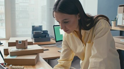 Tilt up shot of young woman bending over desk with laptop while working at shipment office - Powered by Adobe