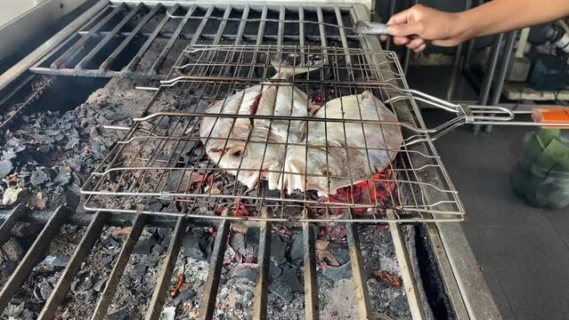 The pompano fish that has been cut in half is grilled over coals using charcoal at restaurant.