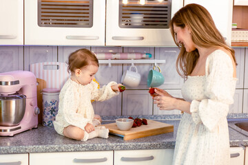 Mom feeding her baby girl with strawberries in the kitchen.