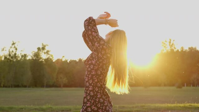 woman in a meadow, happy young girl in the sunlight fixing her hair, breathing fresh air, silhouette in slow motion