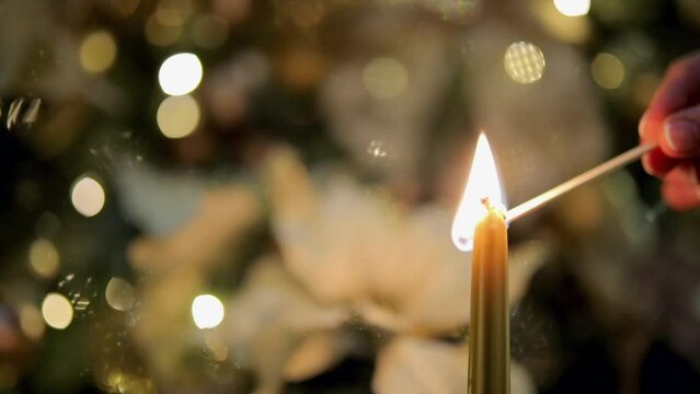 
Lighting the candle and Christmas tree branches with ornaments against bokeh background.