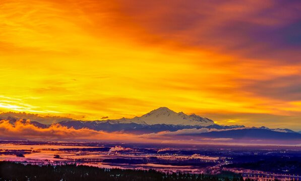 Brilliant orange sunrise over Fraser Valley, BC, Canada, with majestic alpine Mount Baker, USA, on horizon.