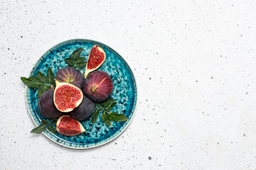 Obraz na płótnie Canvas Sweet ripe figs with green leaves on the plate on white marble background top view, copy space for your design. Healthy tasty food concept.