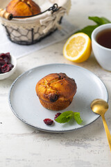 muffins with cranberries on grey plate with cup of tea, lemon and mint