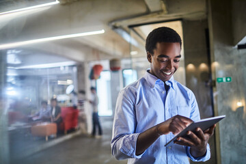 Young African American man using the tablet in a company office - obrazy, fototapety, plakaty
