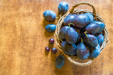 basket of fresh ripe plums on a wooden background