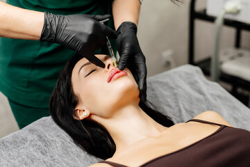 Close-up, woman's lips. A surgeon wearing medical gloves carefully and slowly injects hyaluronic...