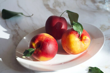 Nectarines lie in a plate on a marble table.