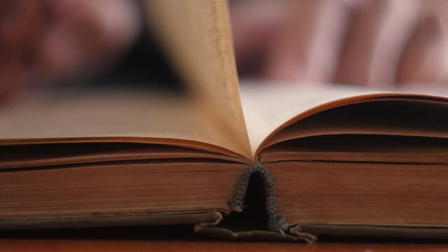 close-up of a page of an old yellowed book being turned over by a man's hand out of focus. selective focus.leisure reading books. old book in the hand of an old man