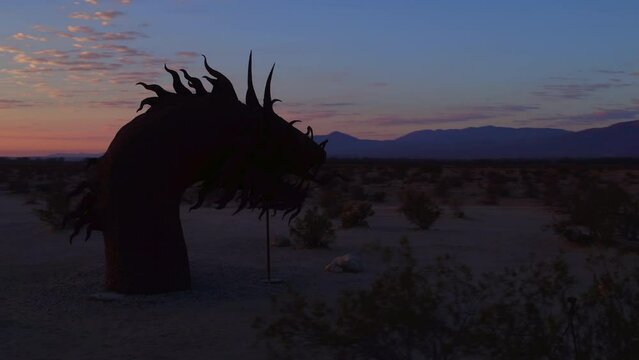 Panning Shot Of Metallic Sculpture Amidst Plants Near Mountains Against Sky During Sunrise - Borrego Springs, California