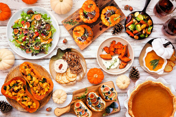 Fototapeta premium Delicious autumn meal table scene. Above view on a white wood background. Stuffed pumpkins and squash, sweet potatoes, appetizers, soup, vegetables and pumpkin pie.