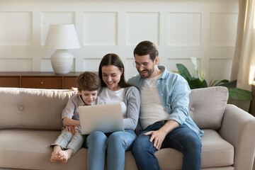 Happy young family with cute little son using laptop at home together, smiling mother and father...
