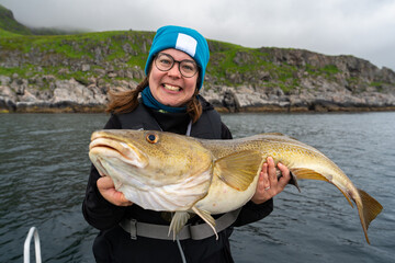 Happy young woman holding big arctic cod. Norway happy fishing. Happy fisherwoman with cod fish in...