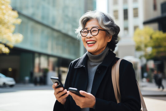 Elderly busy successful beautiful Asian business woman, korean professional businesswoman holding cellphone using smartphone standing or walking on big city urban street outside. Website images