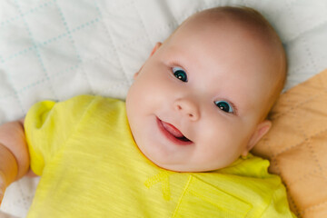 Portrait of a cute newborn girl lying on a bed in a yellow T-shirt