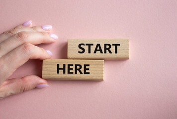 Start here symbol. Wooden blocks with words Start here Beautiful pink background. Businessman hand. Business and Start here concept. Copy space.
