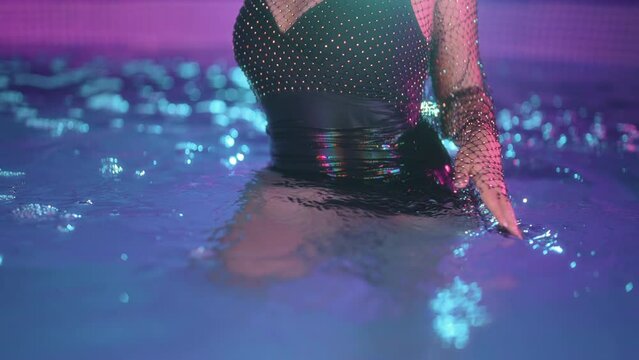 Glamorous woman dancing in pool water party. Shining sexy wearing, night outfit