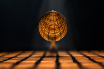 shot of the convex part of a suspended silver spoon reflecting the linear design of the underlying plane, illuminated by a ray of light from above, on a black background