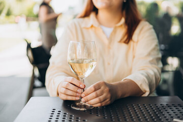 White wine glass in an outdoor cafe. Happy 30s woman sitting on the cafe terrace on the city street. Traveler. Woman hands toasting with wine