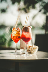 Two long glasses with orange cocktails made from red bermouth on a table next to a bowl of popcorn with an artistically blurred background