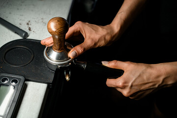 Coffee making process. Woman barista pressing groud coffee with tamper. Close up view.