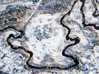 Aerial view on winter river streaming through the field with the tree on it. Everything is covered with snow.