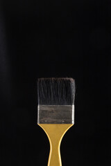 dark brush with yellow handle placed in front of a black background, the bristles are dark and barely contrast